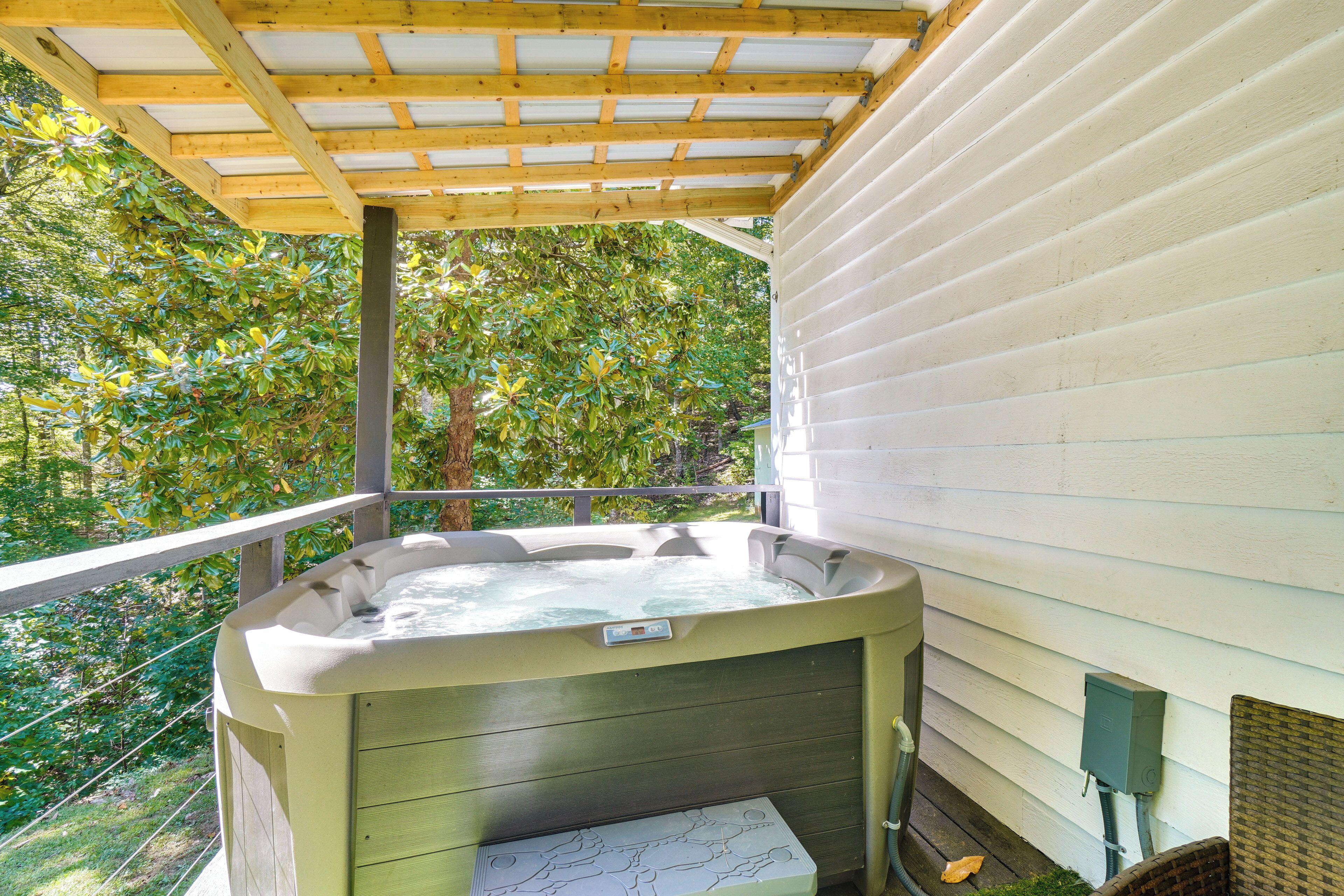 A hot tub under a wooden pergola with a house in the background.