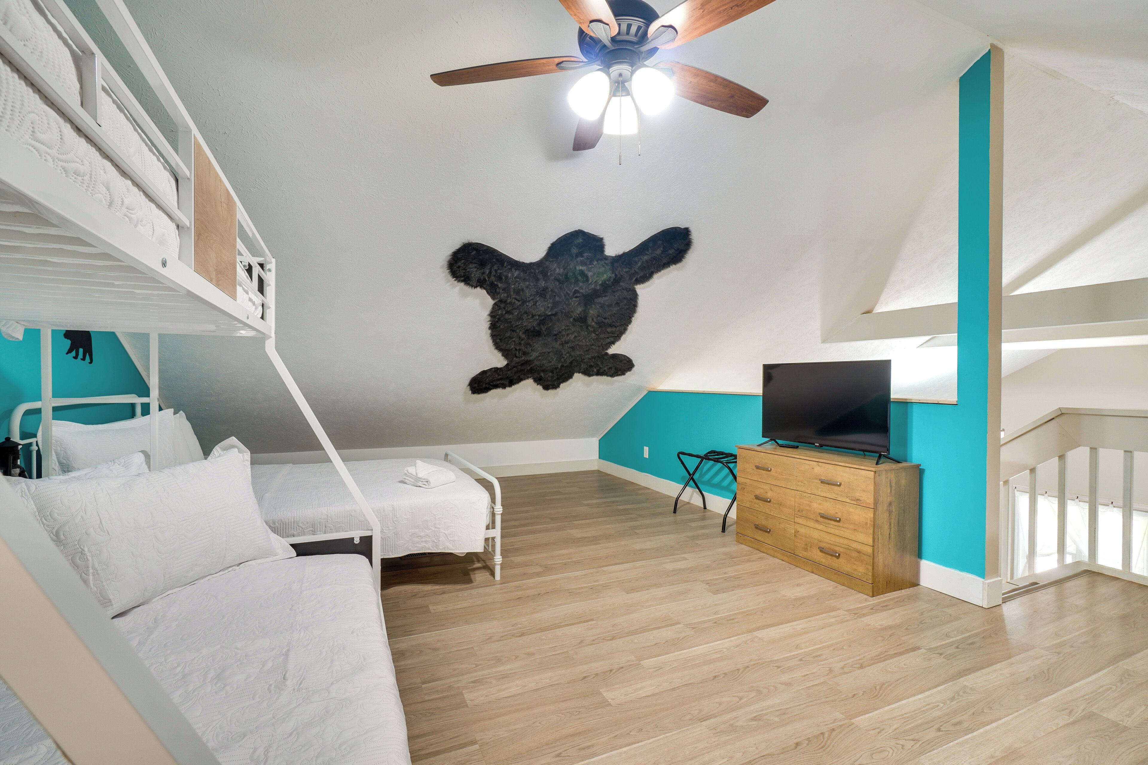 A bedroom with a bunk bed, a ceiling fan, a flat-screen TV, and a wooden dresser.