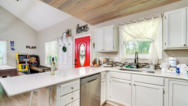 A modern kitchen with white cabinets, a dishwasher, a red door, and a window with sheer curtains. - Smoky Mtn Home w/ Hot Tub: 10 Mi to Dollywood! (Sevierville)
