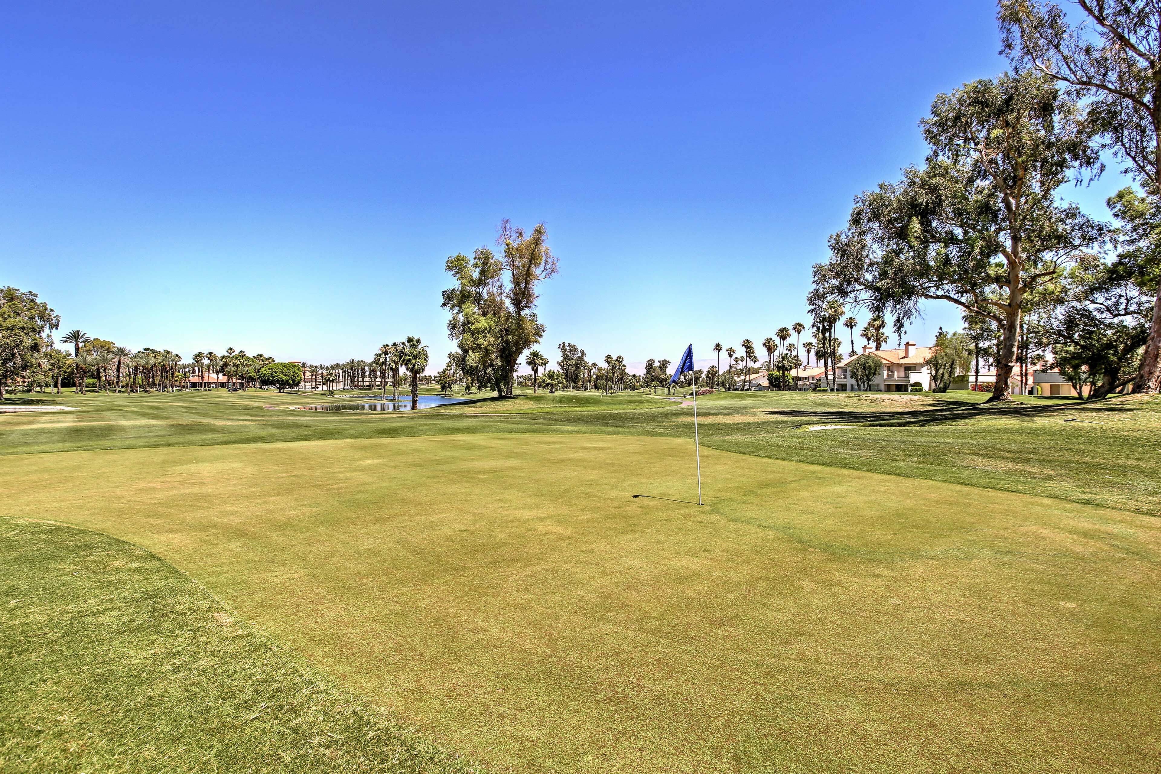 A golf course with a flagstick, trees, and a clear blue sky.