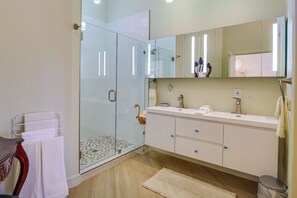 A modern bathroom with a glass shower enclosure, a white vanity with a large mirror, and a wooden floor. - Tennis, Golf & Pools: Lovely Palm Desert Condo! (Palm Desert)