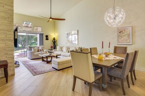 A spacious living room with a dining area, large windows, and a chandelier.