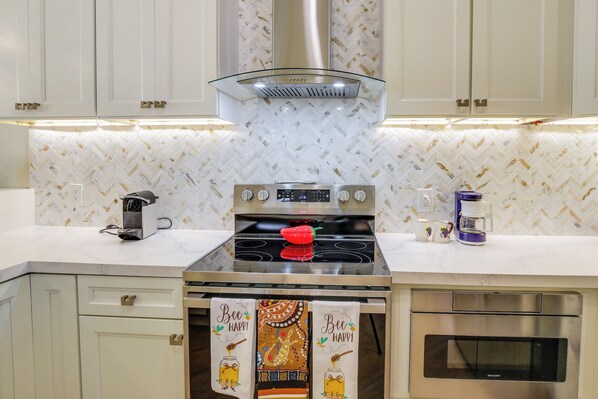 A modern kitchen with a stainless steel stove, a glass range hood, and a herringbone-patterned backsplash.