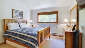 Une chambre à coucher avec un lit en bois, une table de chevet, une commode, un miroir et une fenêtre avec des stores.
