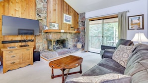 Un salon chaleureux avec une cheminée en pierre, des murs en bois, un grand téléviseur à écran plat et un coin salon confortable avec un canapé et une table basse.