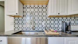 Una cocina con un lavamanos de acero inoxidable, armarios blancos y un salpicadero con diseño.