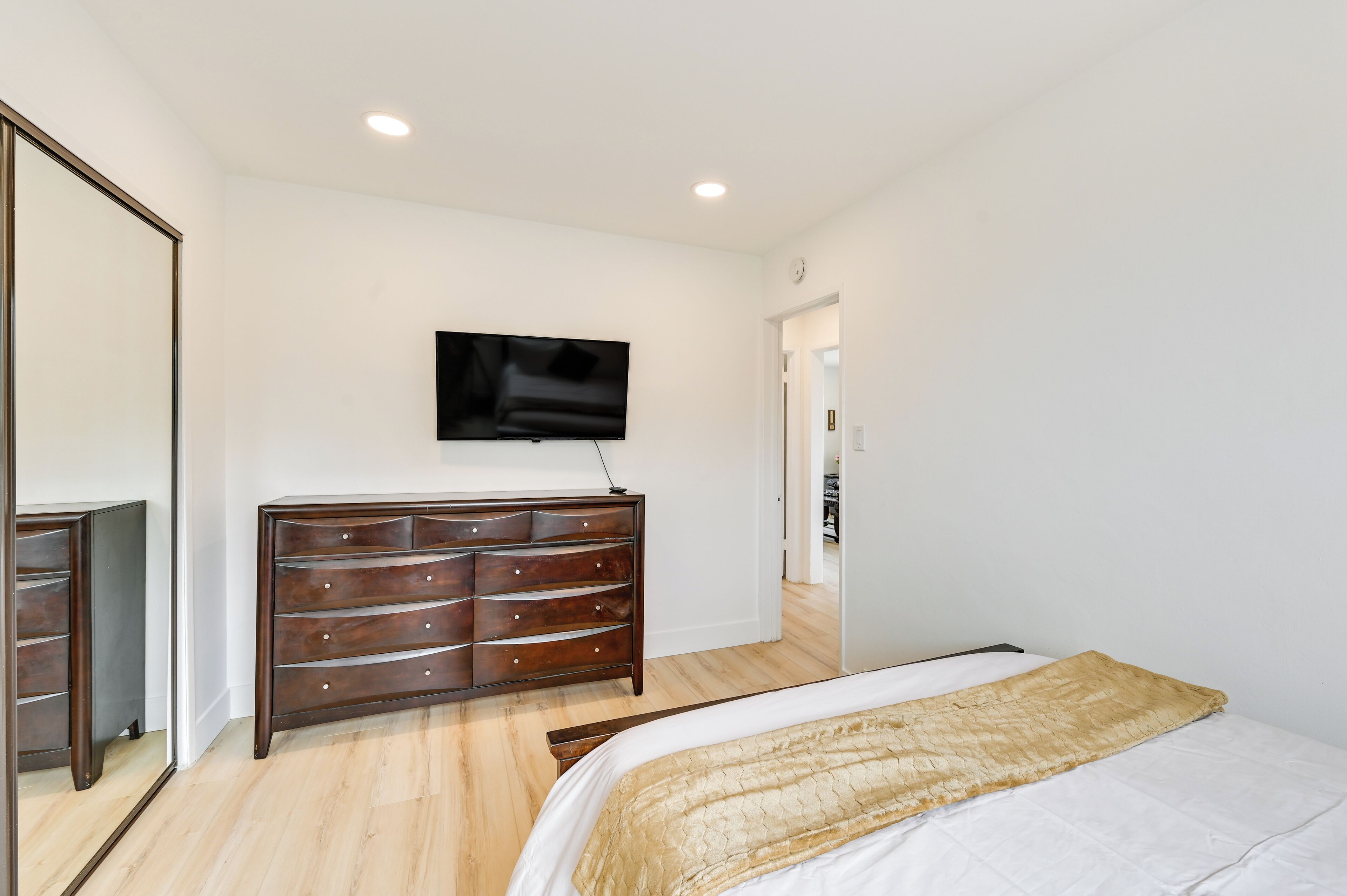 Un dormitorio con cama, cómoda, televisor en la pared y espejo.