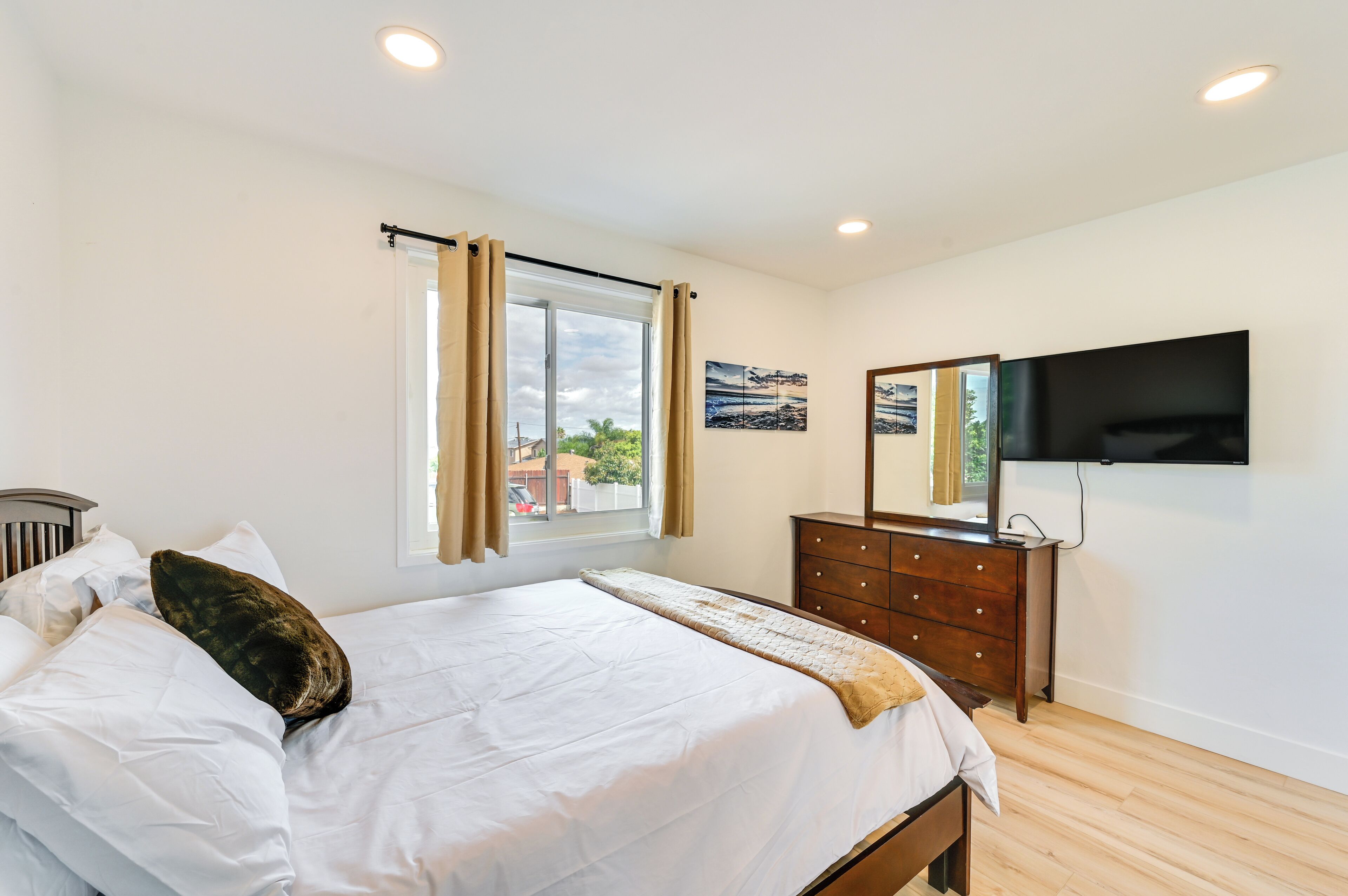 A bedroom with a bed, a dresser, a TV mounted on the wall, and a window with curtains.