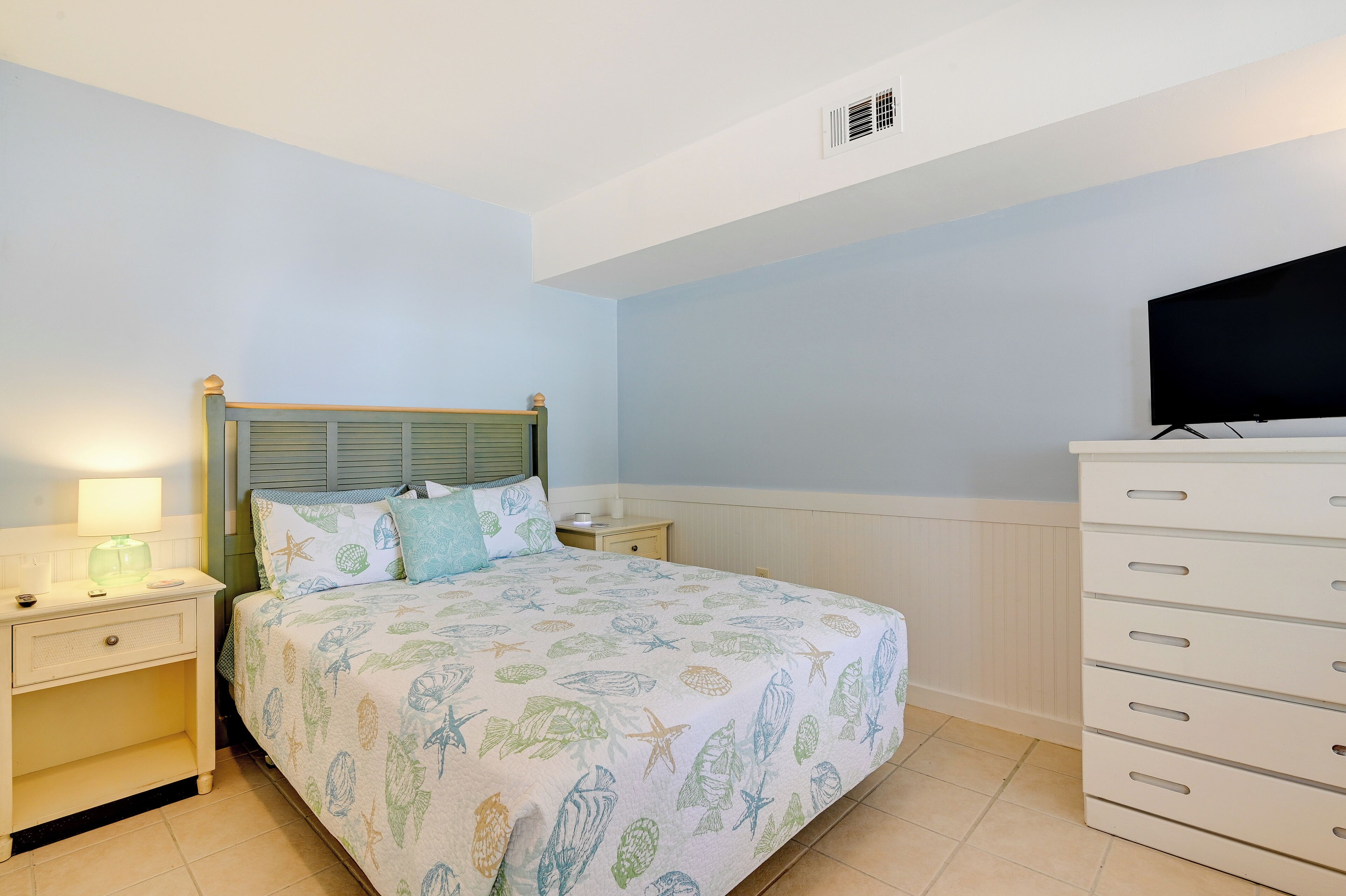 A bedroom with a bed, nightstands, a dresser, and a television.