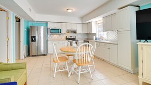 A modern kitchen with white cabinets, a stainless steel refrigerator, a microwave, and a dining table with chairs. - Pawleys Island Retreat (Pawleys Island)