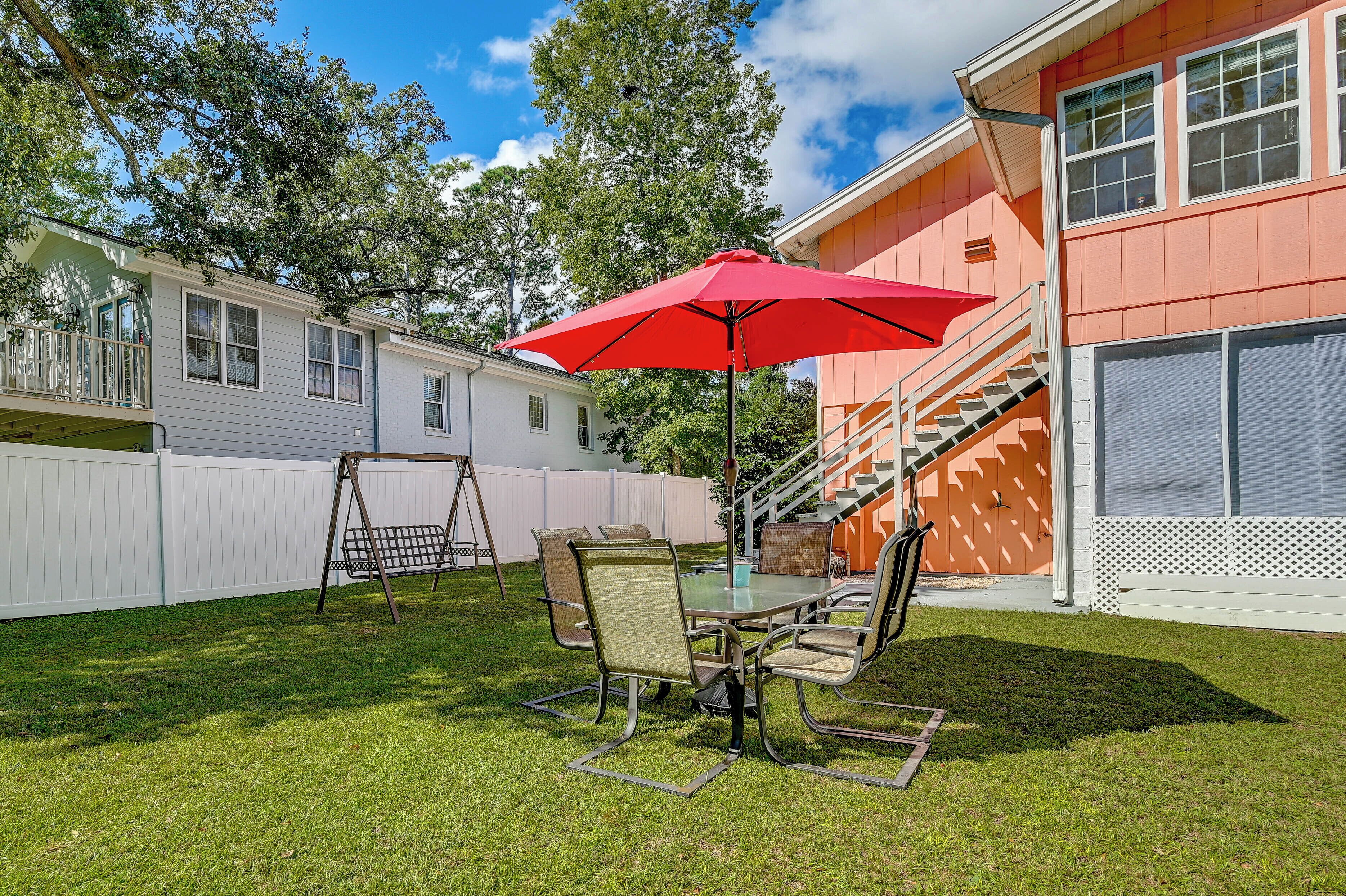 A patio with a table and chairs, a red umbrella, and a white fence.