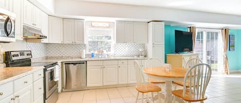 A kitchen with white cabinets, stainless steel appliances, a tiled floor, and a dining area with a wooden table and chairs.
