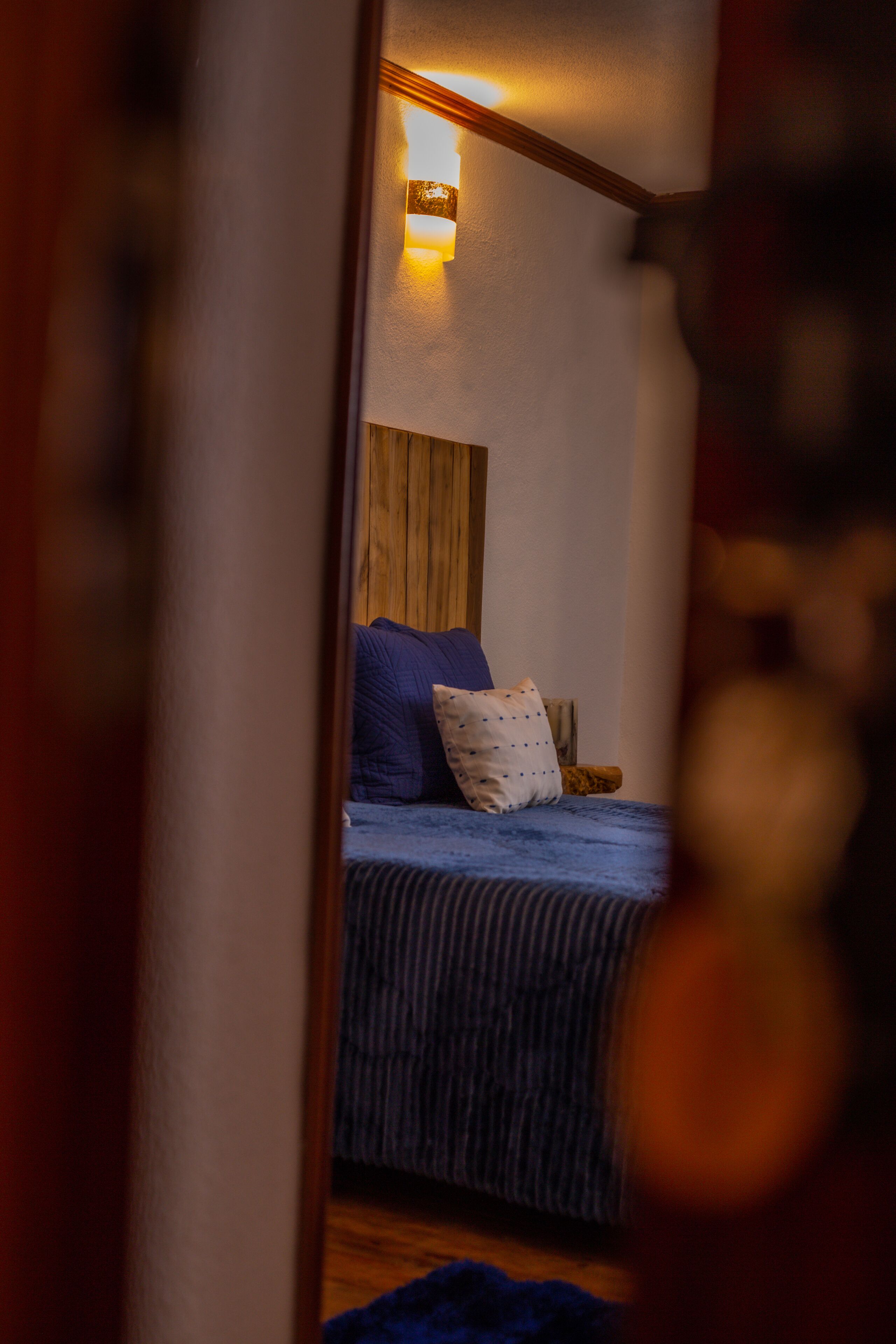 Une chambre à coucher avec une tête de lit en bois, un lit avec une literie bleue et un luminaire fixé au mur.