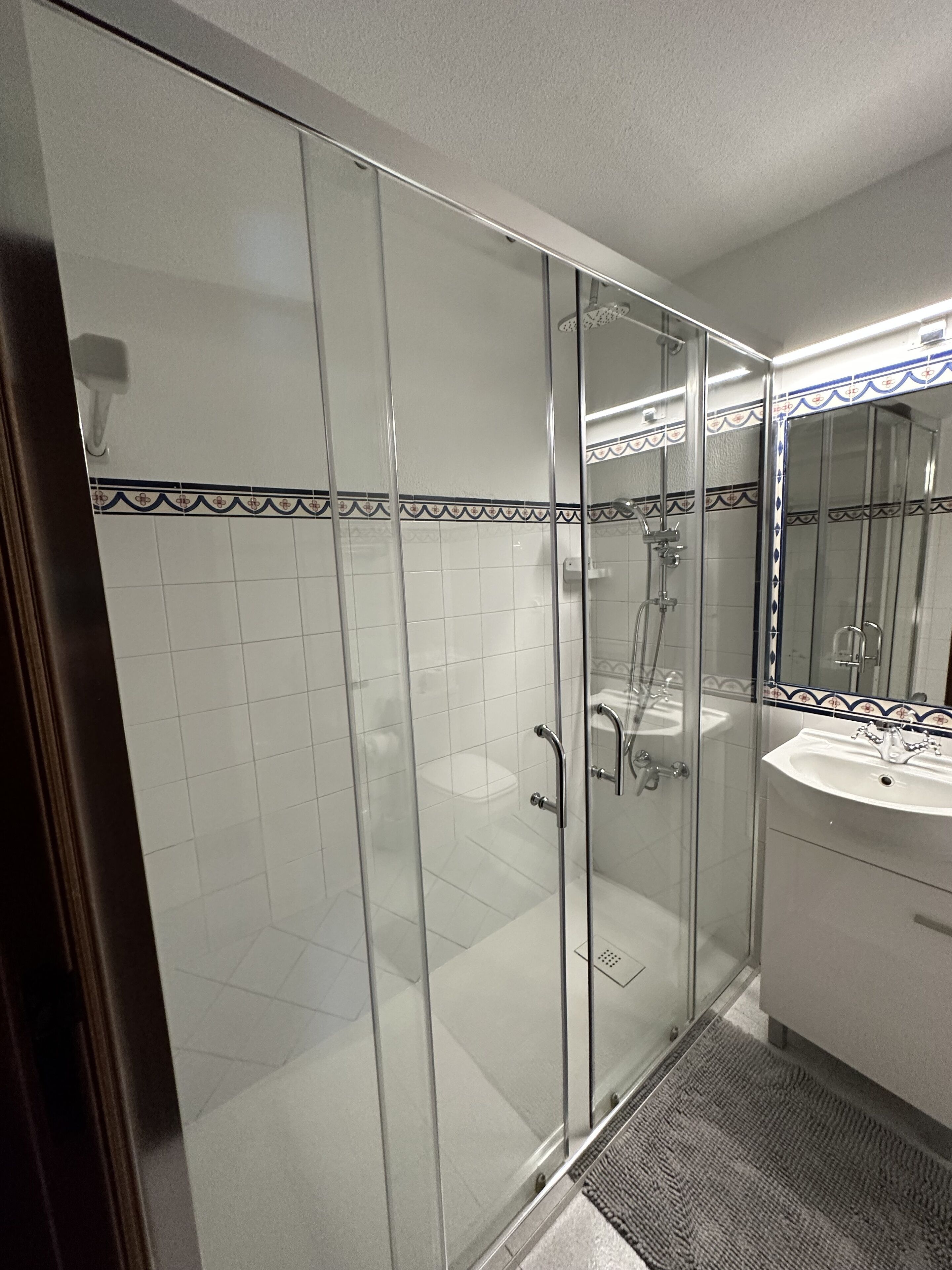 A modern bathroom with a glass shower enclosure, white tiled walls, and a sink with a mirror.