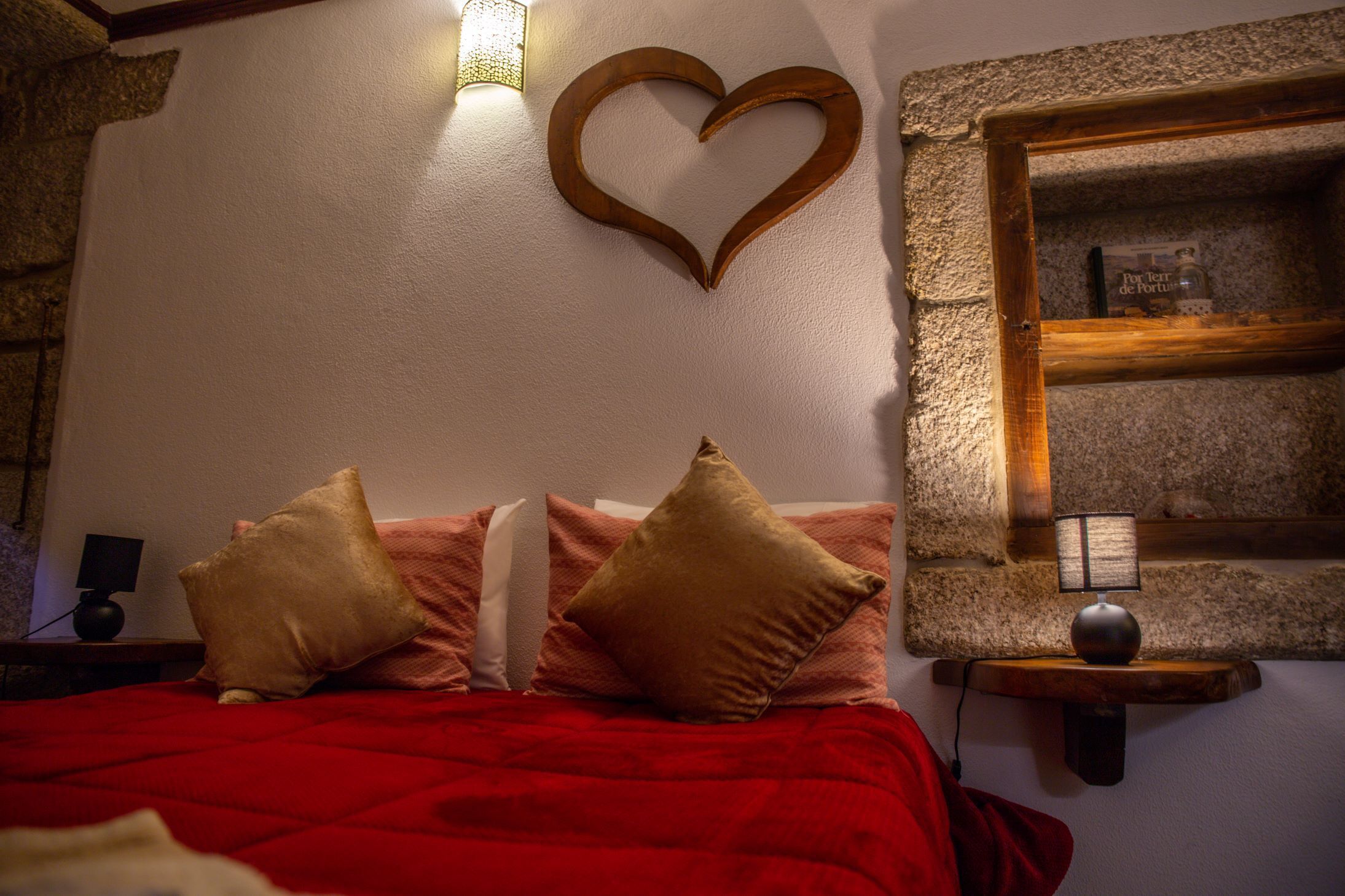 A bedroom with a red bedspread, wooden headboard, and a heart-shaped decoration on the wall.