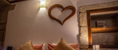 A bedroom with a red bedspread, wooden headboard, and a heart-shaped decoration on the wall.