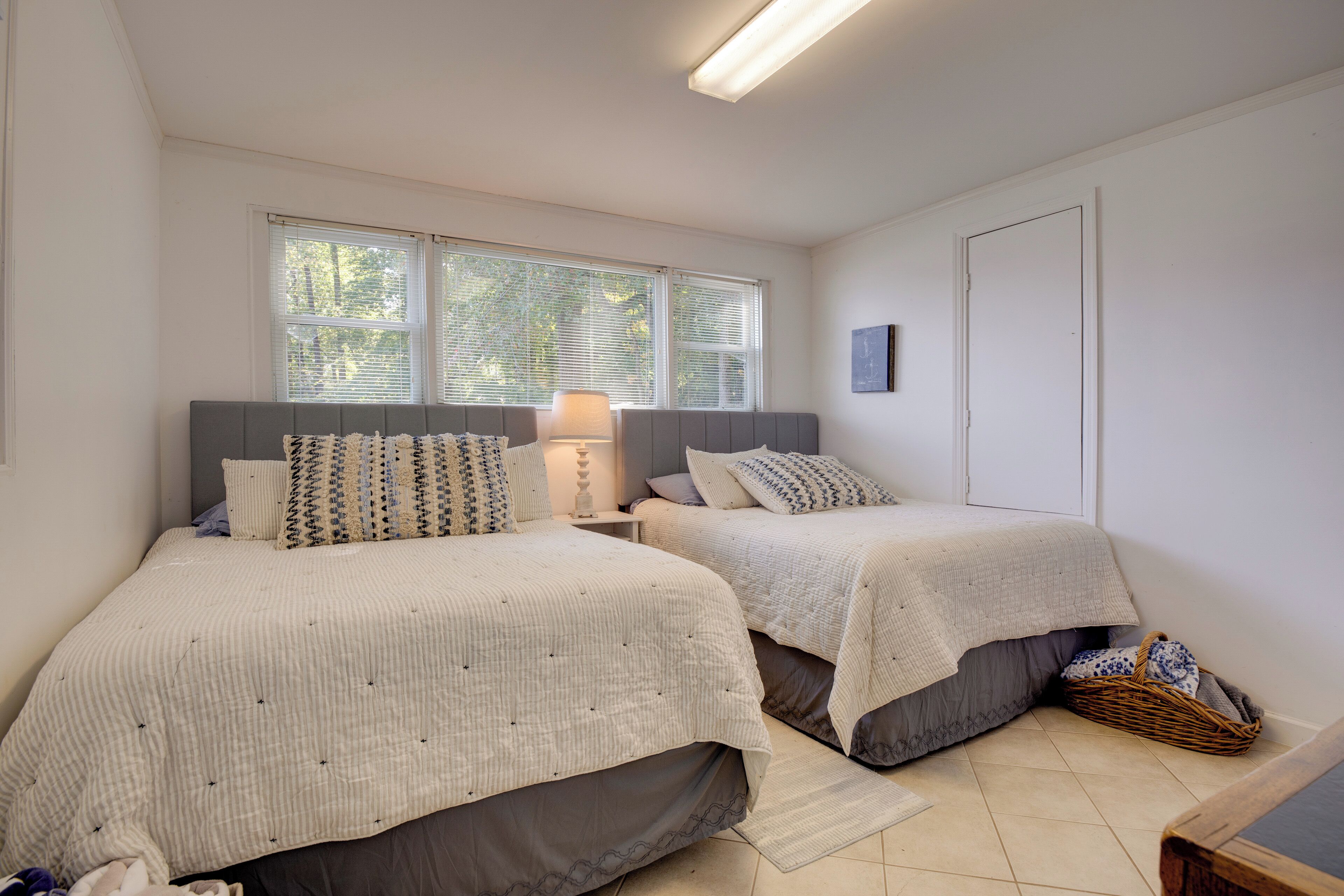 A bedroom with two beds, a nightstand, a lamp, and a window with blinds.