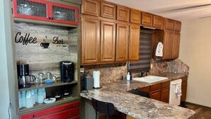 A kitchen with wooden cabinets, a granite countertop, a coffee station, and a sink.