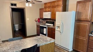 A compact kitchen with wooden cabinets, a white refrigerator, a microwave, and a gas stove.