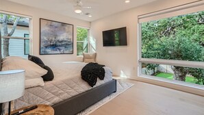 A modern bedroom with a large bed, a flat-screen TV, and a view of a garden through a large window. - Custom New Build Central Austin Home Mins to DT (Austin)