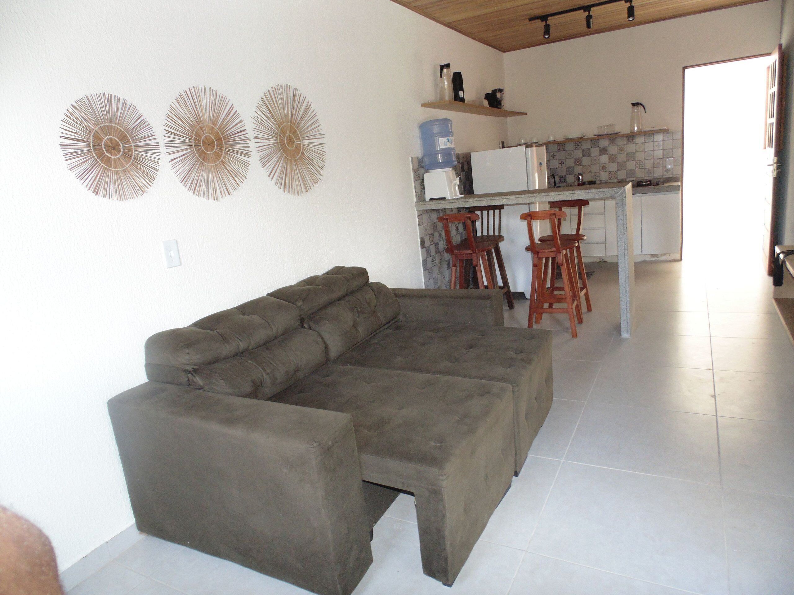 Una sala de estar con un sofá modular, una cocina con un refrigerador blanco y un dispensador de agua.