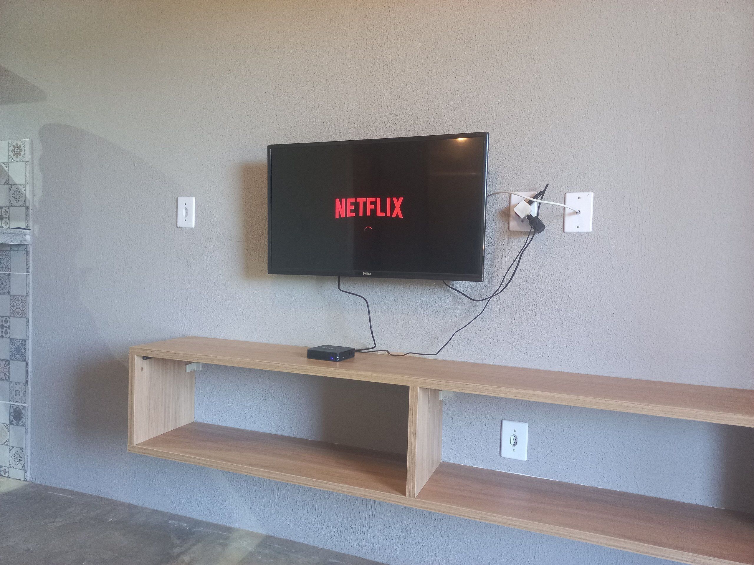 A flat-screen TV mounted on a wall with a wooden shelf below.