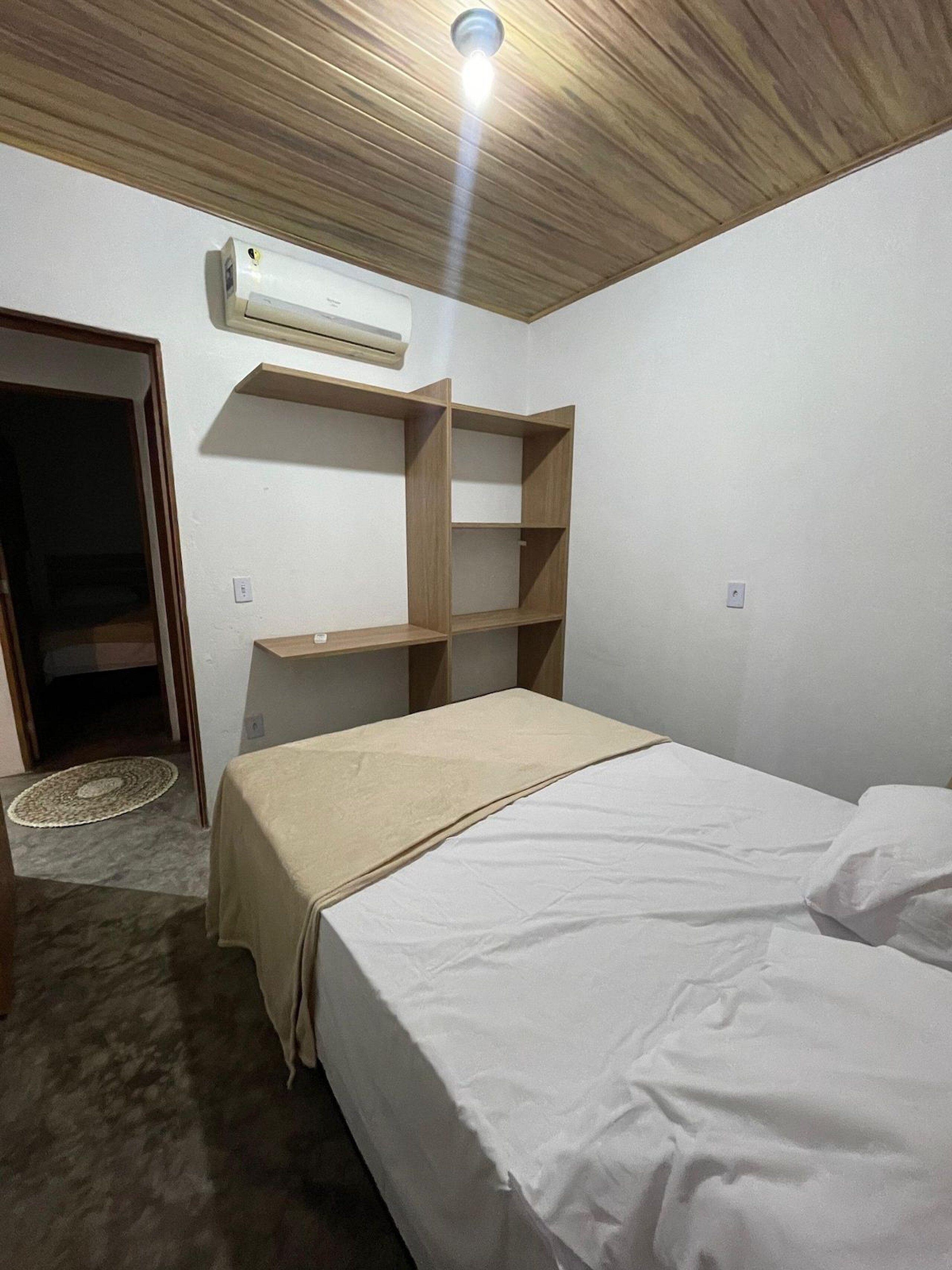 A bedroom with a bed, wooden shelves, an air conditioning unit, and a door.