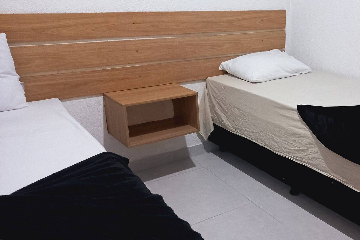 A small, clean room with two single beds, a wooden nightstand, and a white wall.