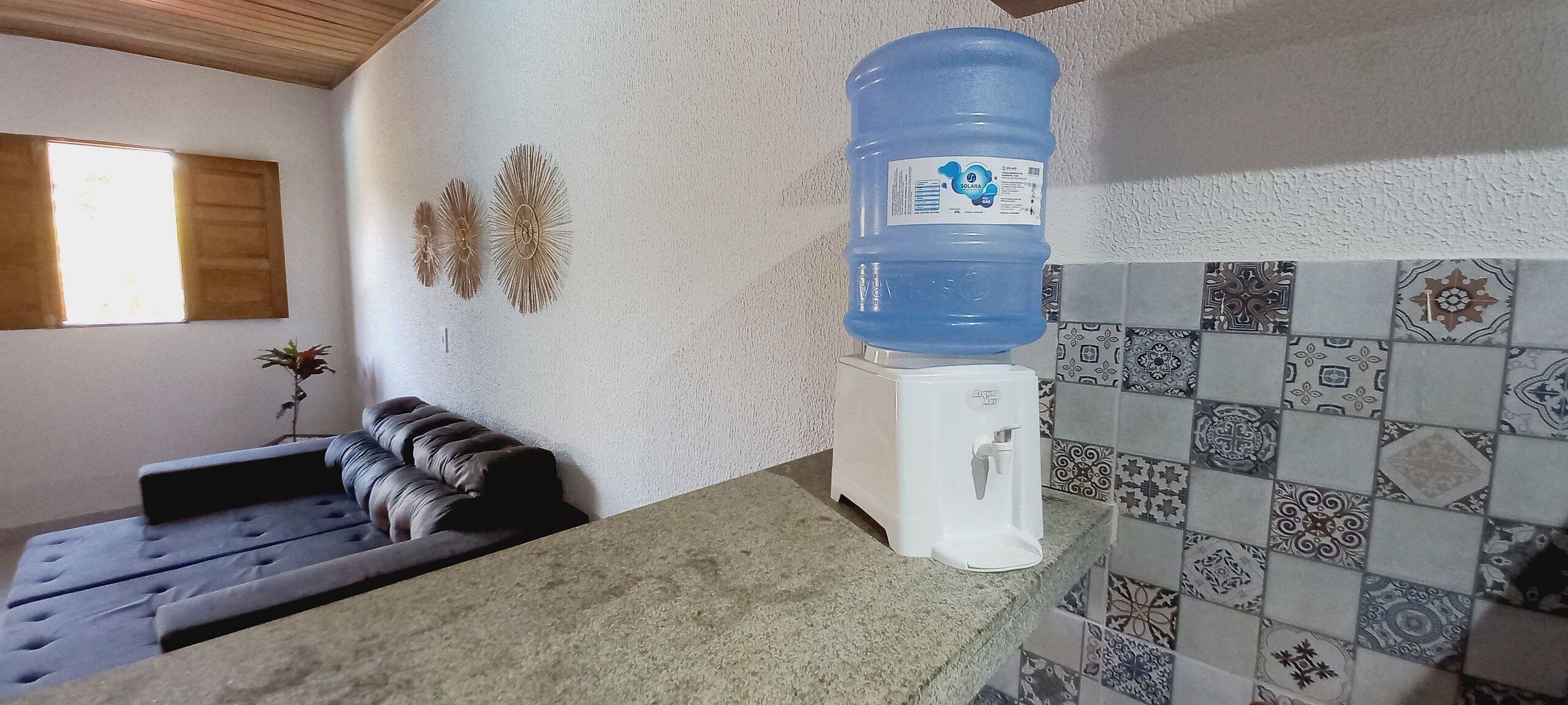 Un baño con dispensador de agua, un depósito grande de agua, un banco acolchado, detalles decorativos en la pared y azulejos con diseño.