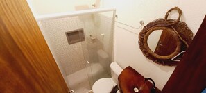 A bathroom with a glass shower enclosure, a toilet, and a wicker basket on the wall.