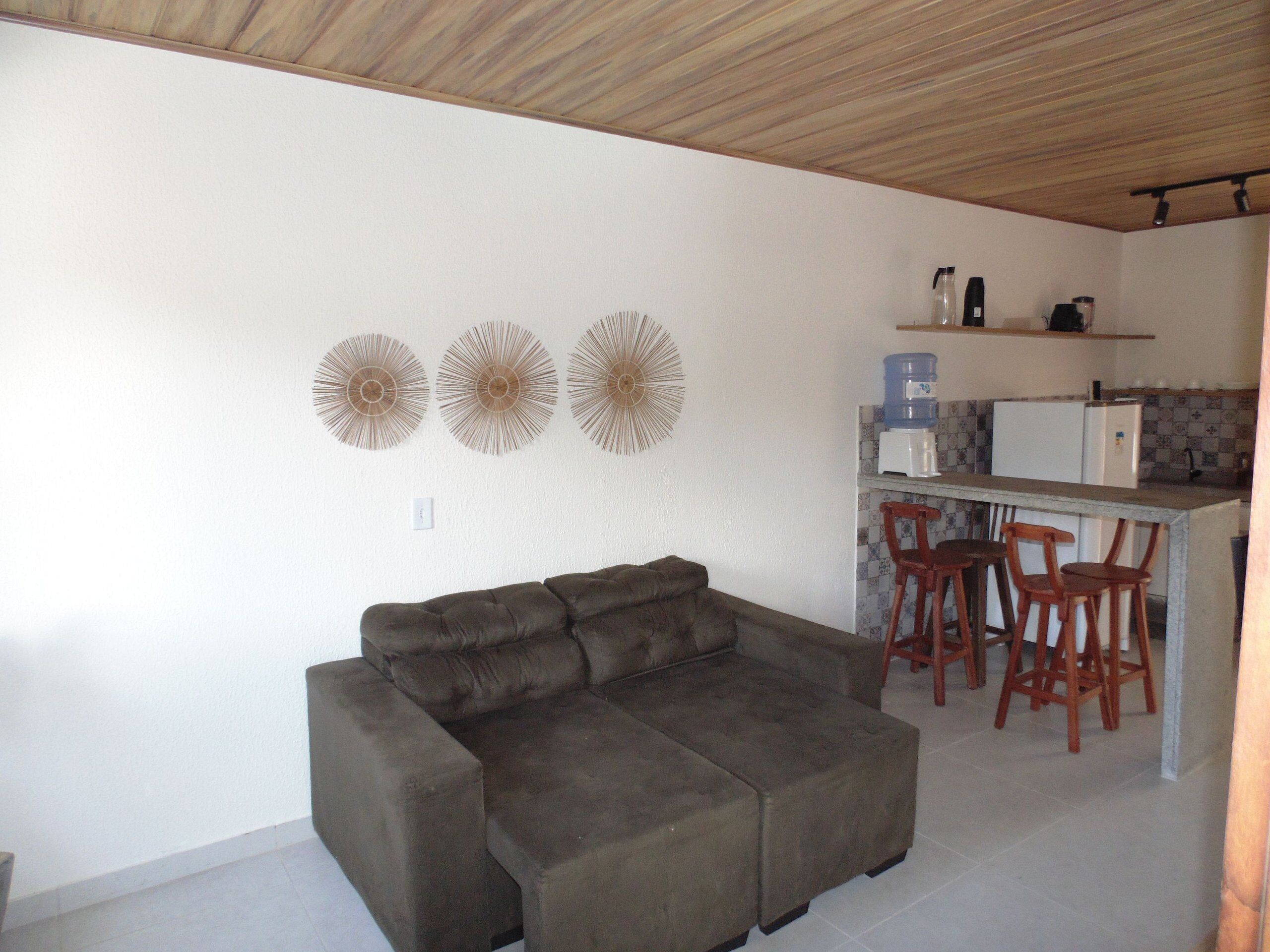 A living room with a sofa and a kitchen area with a bar and stools.