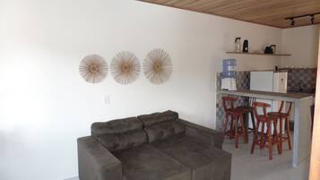 A living room with a sofa and a kitchen area with a bar and stools.