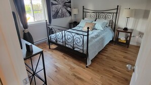 Une chambre à coucher avec un lit, deux tables de chevet, un bureau et une fenêtre avec des rideaux.