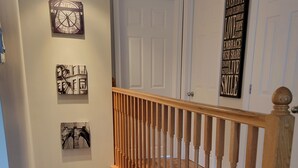 Un escalier en bois avec une rampe, une horloge et des œuvres d’art murales inspirantes.