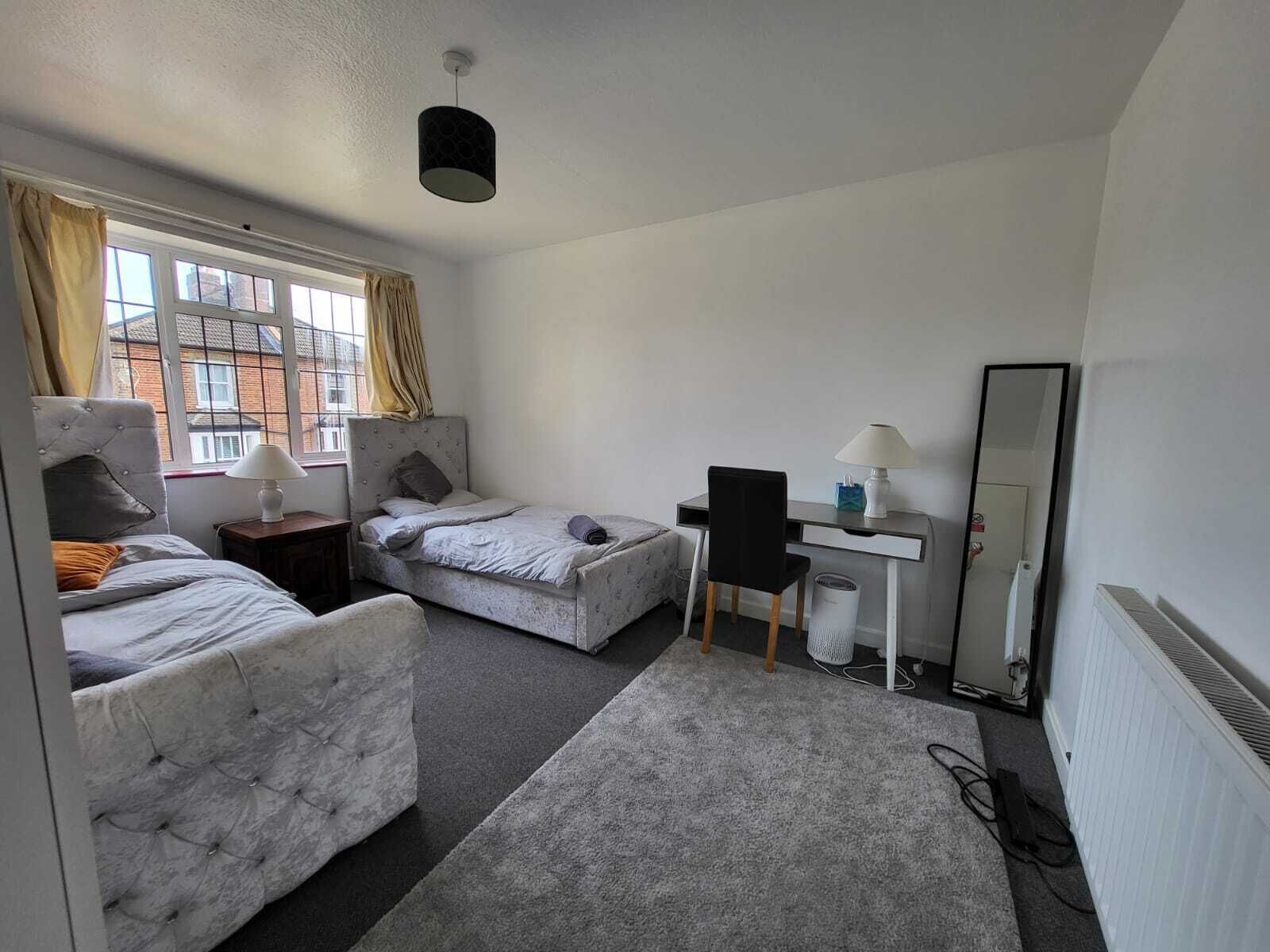 Une chambre d’hôtel de taille modeste, équipée de deux lits, d’un bureau, d’une chaise, d’une lampe et d’un miroir.