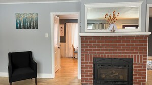 A living room with a fireplace, a black armchair, and a painting on the wall. - Beautiful 3 BR Cedar Ranch Home with Awesome Master and Cooks Kitchen  (Colchester)