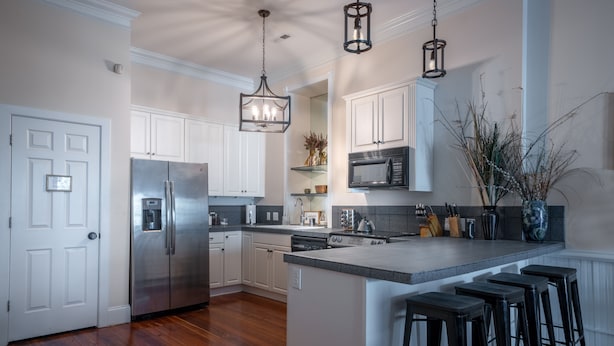 Una cocina moderna con armarios blancos, electrodomésticos de acero inoxidable y una isla central con taburetes de bar.