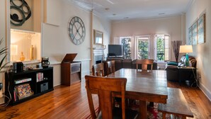 Amplia sala de estar con una mesa de comedor de madera, asientos cómodos, una chimenea y un reloj grande en la pared.