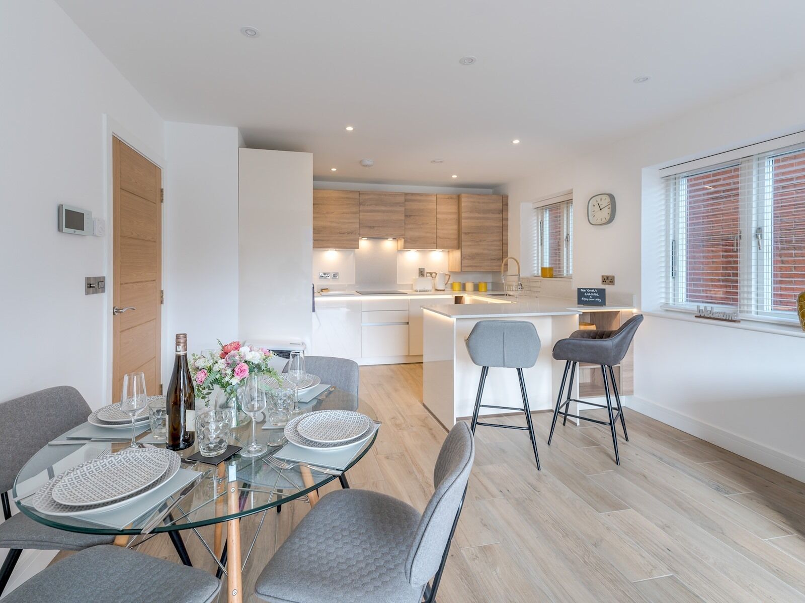 Een moderne keuken met witte kasten, een centraal eiland en een eetgedeelte met een glazen tafel en grijze stoelen.