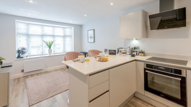 A modern kitchen with a central island, built-in oven, and a dining area with two chairs.
