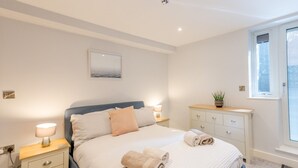 A bedroom with a bed, bedside tables, a dresser, a window, and a wall-mounted artwork.