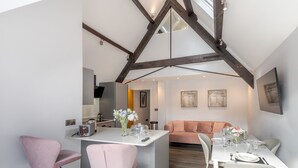 Et moderne køkken med en central ø, et spiseområde med et bord til fire personer, og en opholdsstue med sofa og kunstværker.