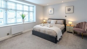 Un dormitorio moderno con un ventanal grande, una cama con cabecera oscura, mesitas de noche con lámparas y una silla.