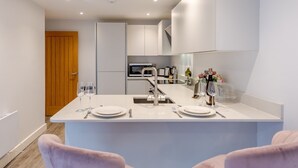 Una cocina moderna con armarios blancos, una isla central con asientos y una puerta de madera al fondo.