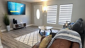 A living room with a brown leather sofa, a white coffee table, a patterned rug, a flat-screen TV mounted on the wall, and a door with a circular window. - Backyard Oasis, calm, quiet and peaceful. Just pack and come enjoy.  (Port St. Lucie)