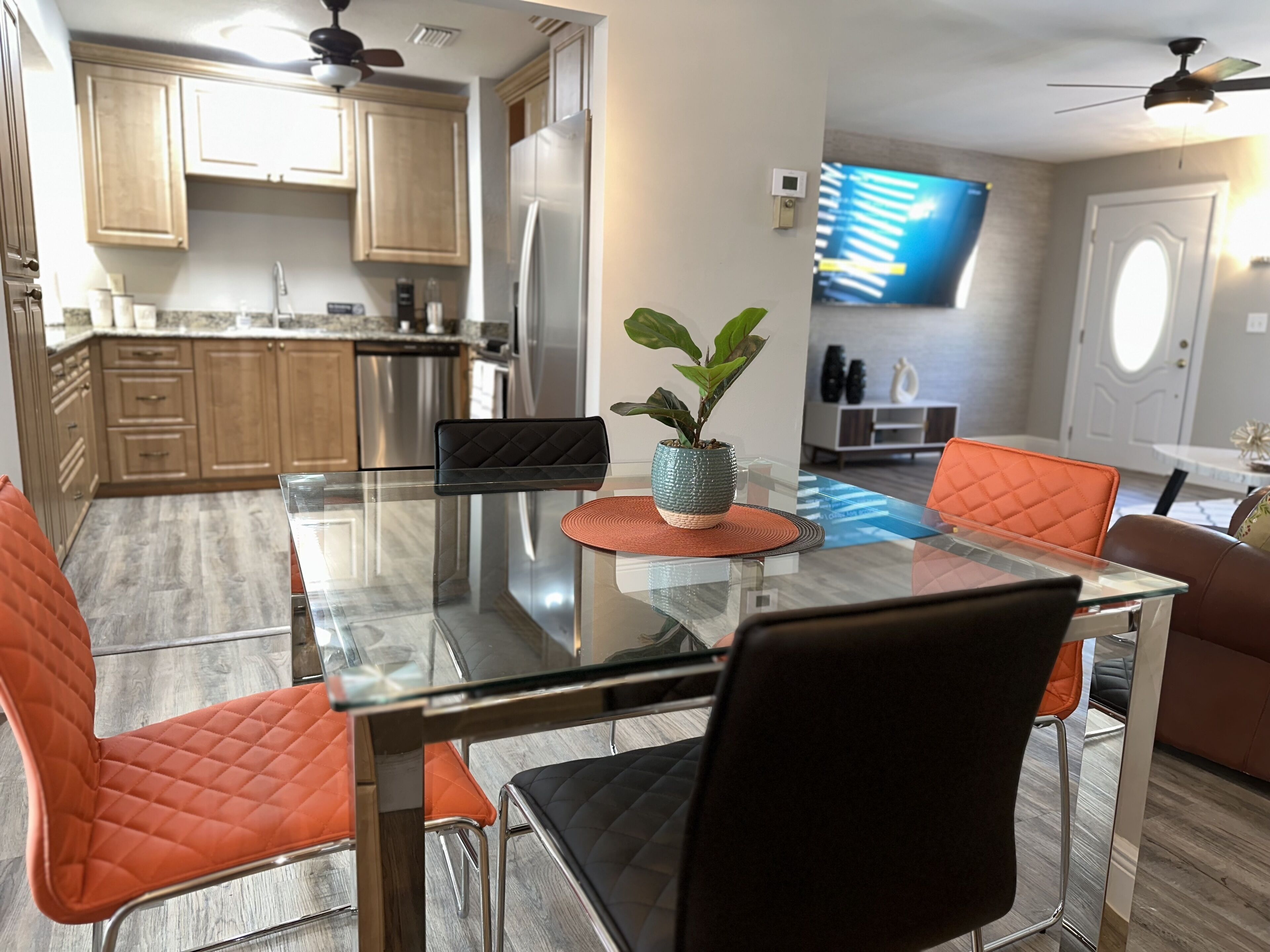 A modern kitchen with wooden cabinets, stainless steel appliances, and a dining area with glass tables and cushioned chairs.