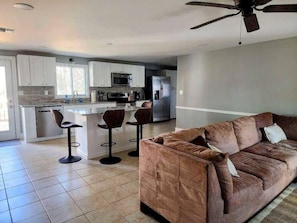 A modern kitchen with a central island, bar stools, and a brown sofa in a living area.