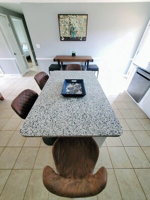 A dining area with a granite table, leather chairs, and a painting on the wall.
