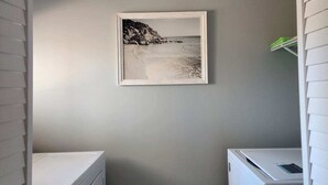 Une buanderie avec un tableau représentant une scène de plage accroché au mur, un lave-linge blanc et un sèche-linge blanc.