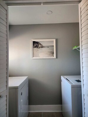 A laundry room with a wall-mounted picture of a beach scene, a white washing machine, and a white dryer.